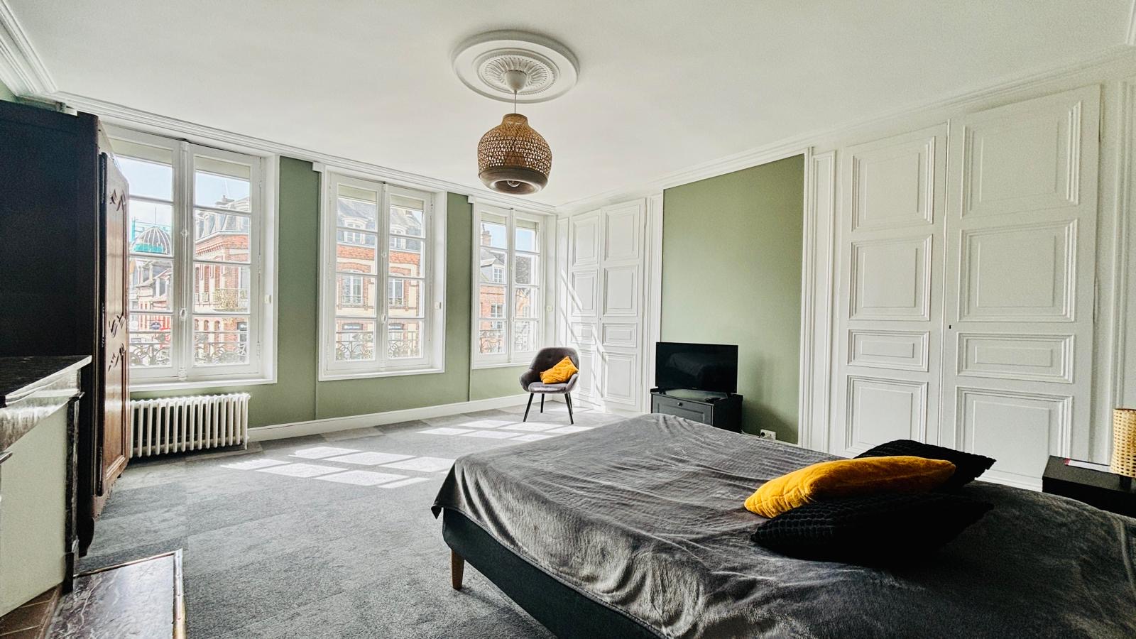 Grande chambre lumineuse aux murs vert d'eau avec vue sur les toits de L'Aigle